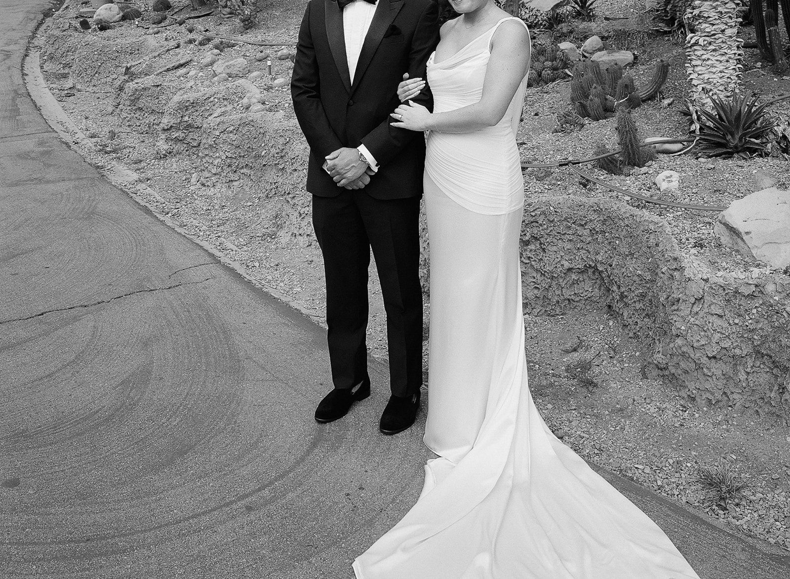 Couple in formal attire posing outdoors, with a long white gown and black tuxedo.