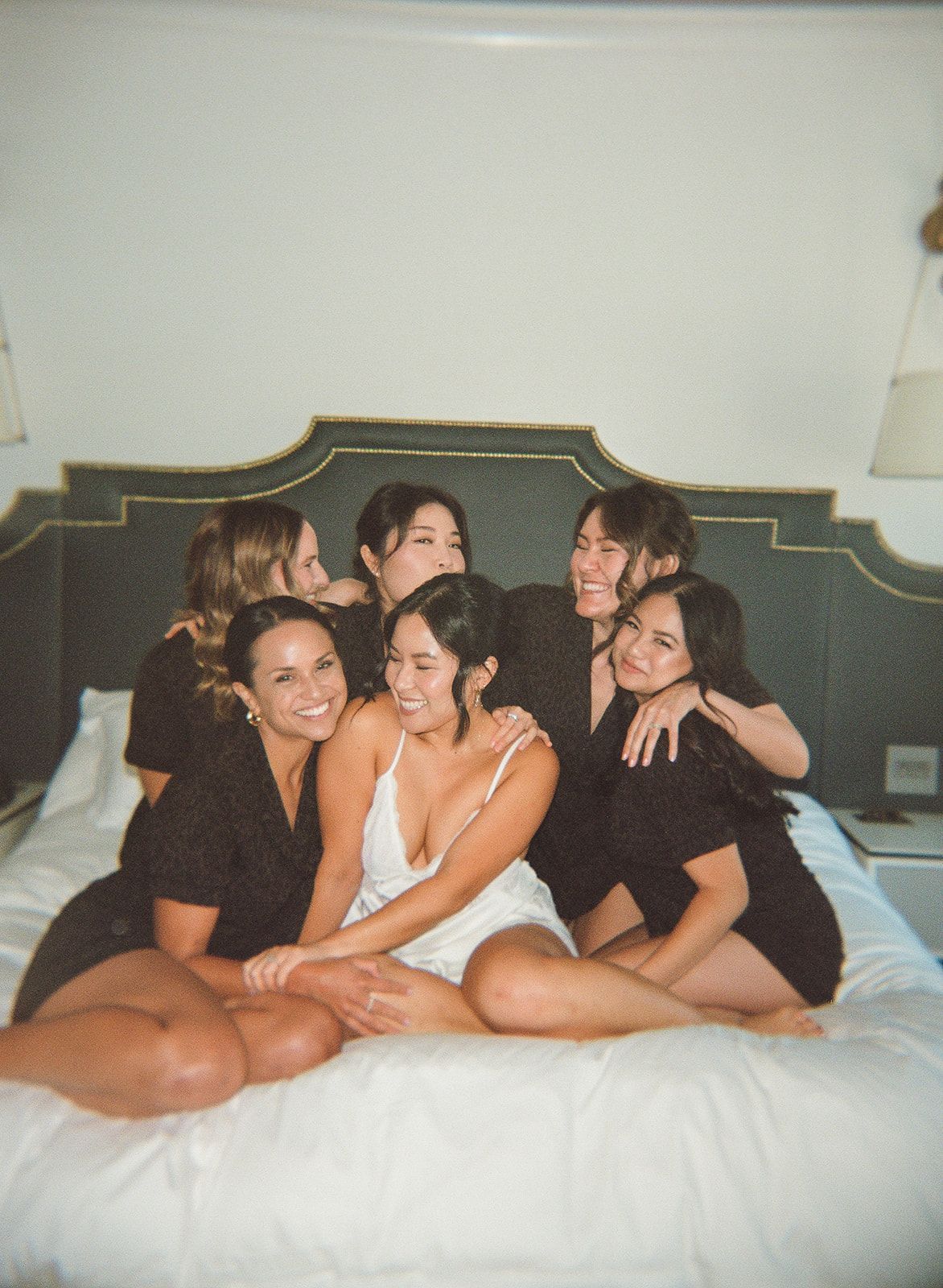 Five people posing on a bed in black and white underwear, smiling in a bedroom.