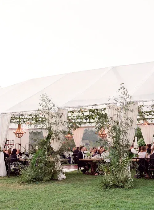 Guests seated under a white tent with greenery decorations at an outdoor event