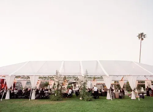 Large white event tent with seated guests on a grassy lawn, decorated for an outdoor celebration.