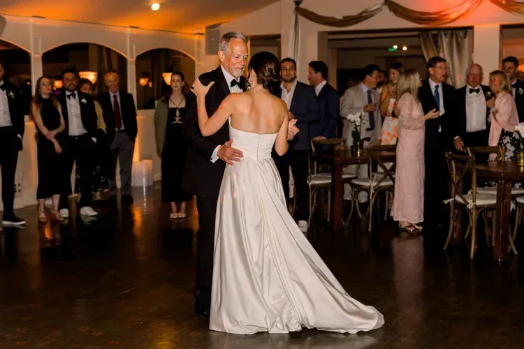Bride and groom dancing at a wedding reception with guests watching nearby.