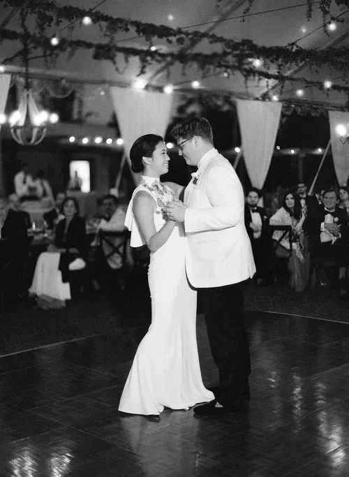 Couple dancing closely at a formal reception under string lights, guests seated in the background