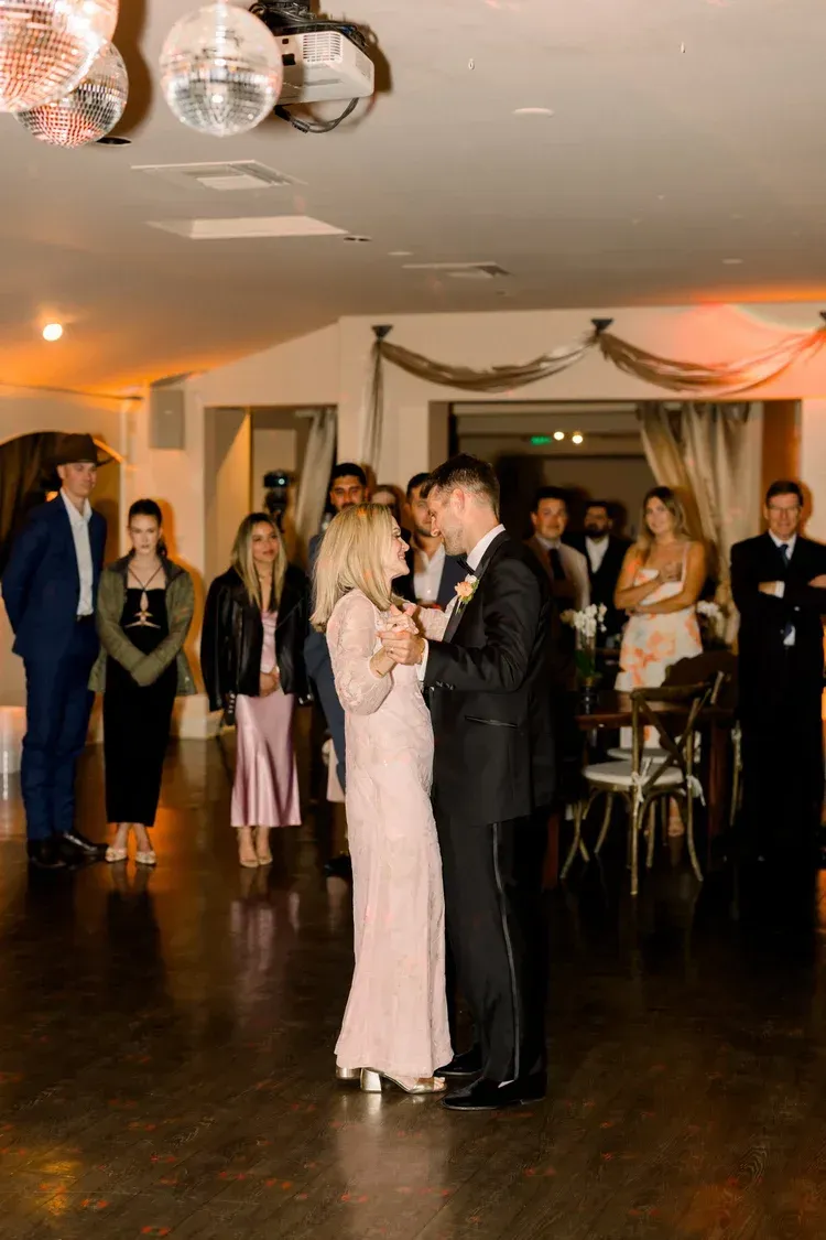 Couple slow dancing in a decorated reception hall with guests watching nearby
