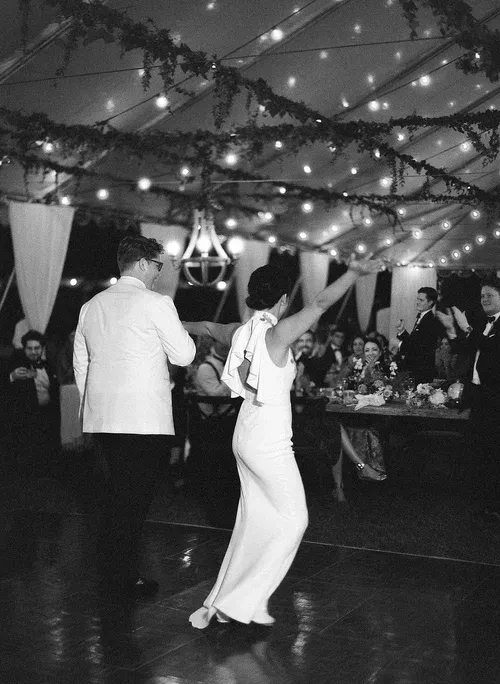 Woman dancing at a festive indoor event under string lights, with guests seated nearby.