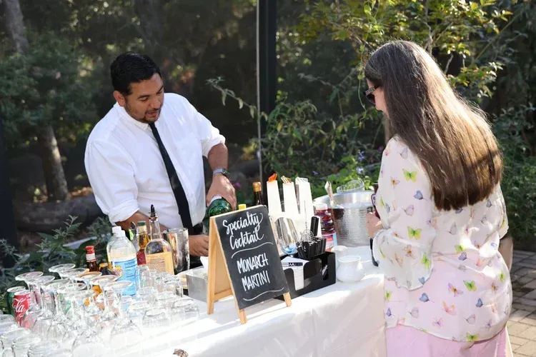 Outdoor drink station with a bartender serving a guest at a decorated table in a garden setting