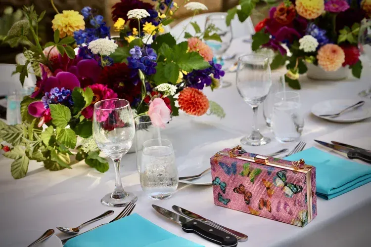 Elegant table setting with colorful floral centerpieces, glassware, and folded blue napkins on a white tablecloth