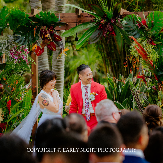 Outdoor wedding ceremony with bride in white and groom in red amid tropical greenery