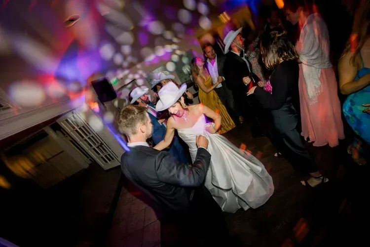 Couple dancing at a formal party under colorful lights, with guests in the background.
