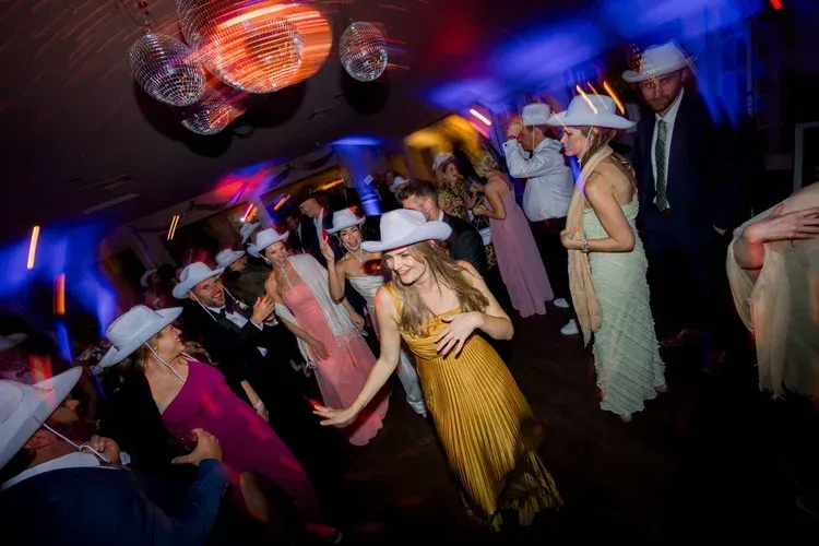 Crowded dance floor with people in white hats dancing under colorful club lights