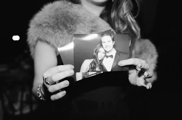 Hands holding a small black-and-white photo at a dark event.