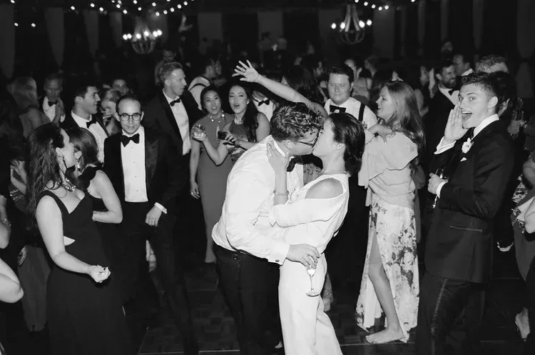 Couple kissing on a dance floor at a formal black-and-white celebration, guests watching around them
