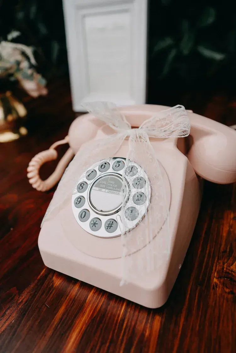Pink vintage rotary telephone on a wooden table, tied with a lace bow
