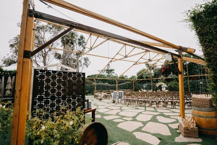 Outdoor patio with geometric wooden canopy, mosaic stone floor, chairs, and potted plants.
