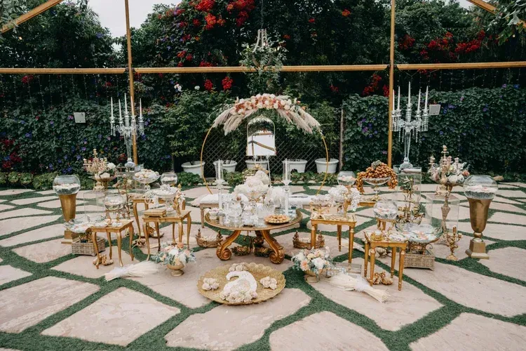 Outdoor wedding reception setup with gold chairs, white floral arch, and candlelit tables on a stone courtyard