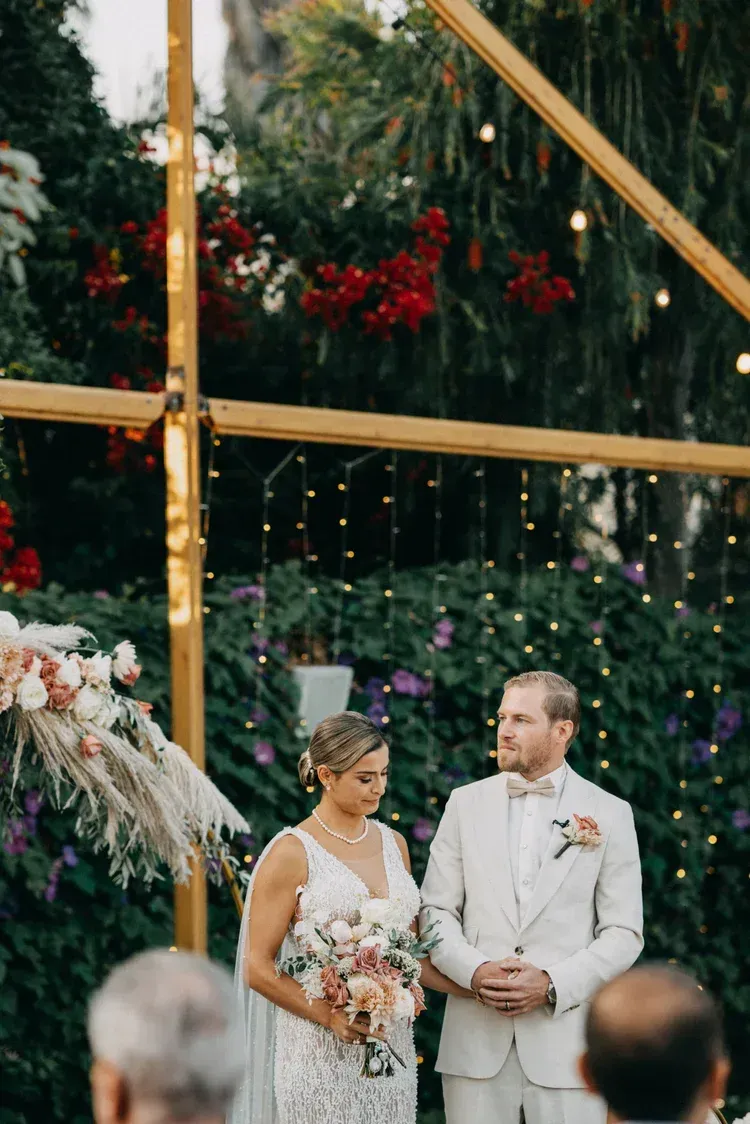 Bride and groom standing at an outdoor wedding ceremony with floral and string-light decor