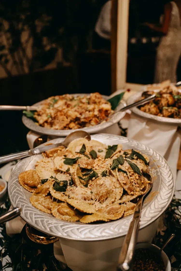 Assorted pasta dishes in ornate white serving bowls, garnished with herbs, on a buffet table