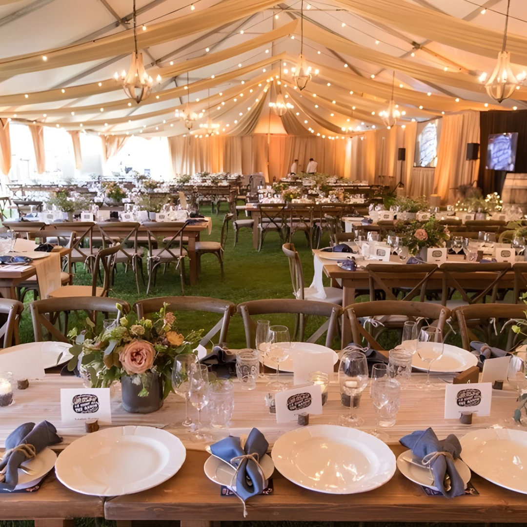 Elegant tented event hall with banquet tables, white table settings, floral centerpieces, and warm string lights
