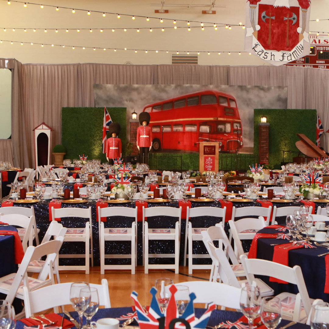 Decorated banquet hall with red, white, and blue table settings and a large red double-decker bus backdrop