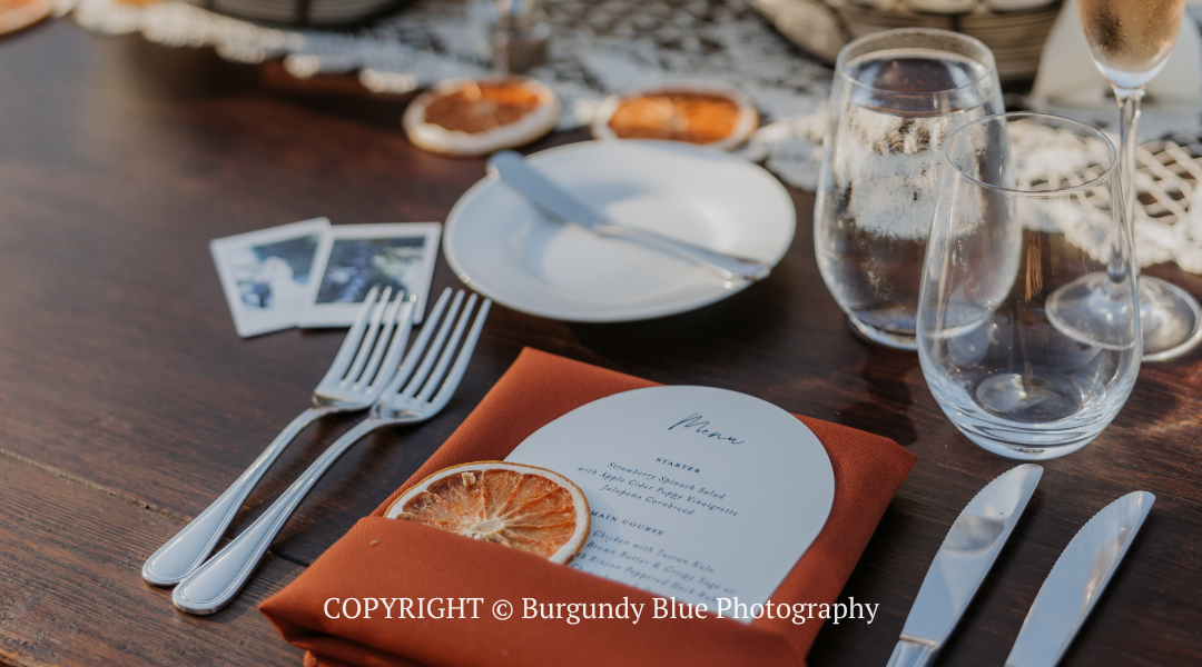 Set table with menu, silverware, water glasses, and orange slice centerpiece on a wooden table