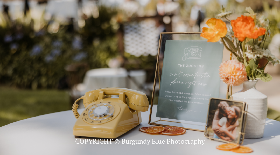 Vintage yellow telephone beside a framed sign, flowers, and a small photo on an outdoor table