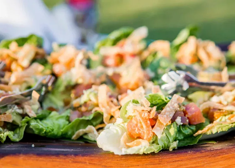 Fresh salad wraps topped with greens, diced tomatoes, and toppings on a wooden table