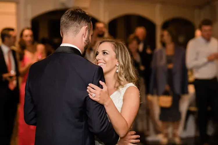Couple dancing at a formal event, smiling and facing each other in a warmly lit ballroom.