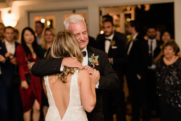 A couple slow dancing at a formal event, with guests blurred in the background.