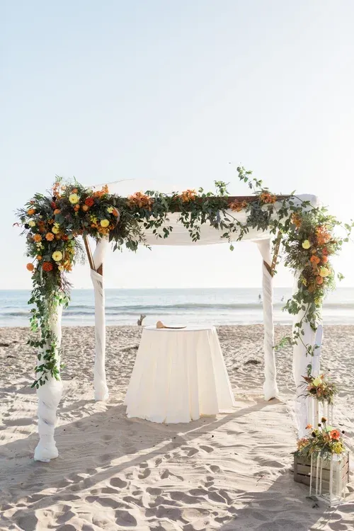 Flower-decorated beach wedding arch with draped white table by the ocean