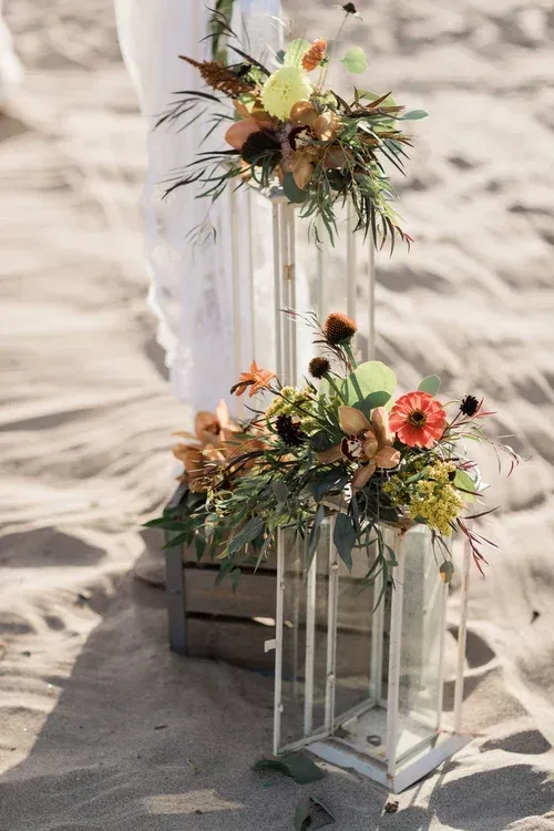 Floral arrangements with white lanterns on sandy ground in bright sunlight