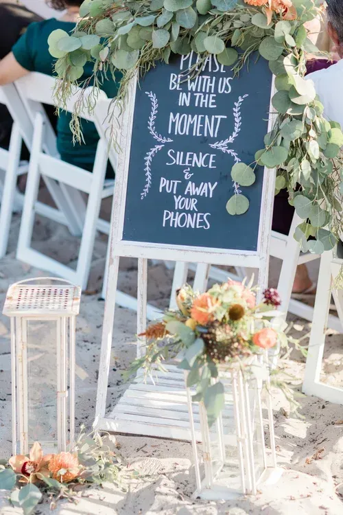 Wedding sign on easel with white lanterns and blush floral arrangement outdoors