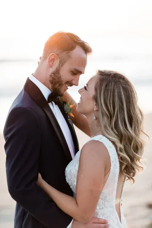 Couple embracing at sunset on the beach, smiling in wedding attire