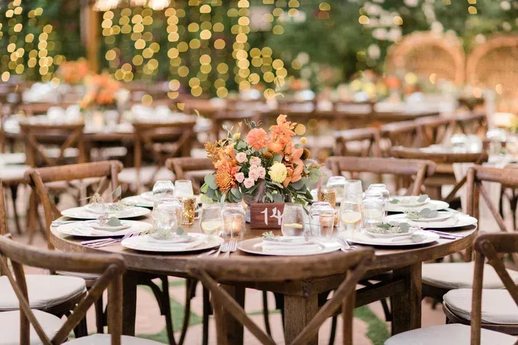Outdoor wedding reception tables with floral centerpieces, candles, and warm string lights at dusk