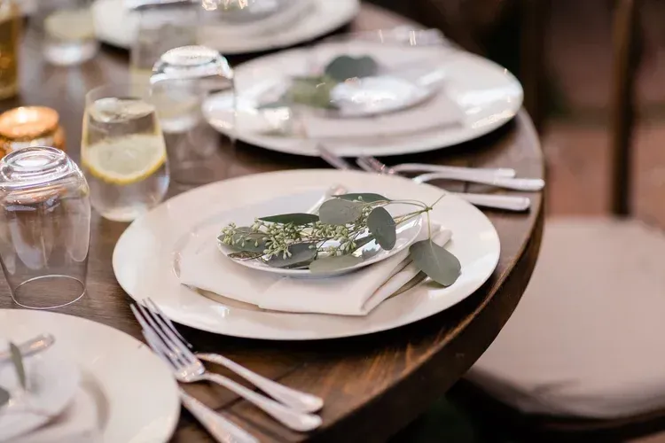 Elegant place settings with white plates, folded napkins, silverware, and water glasses on a wooden table
