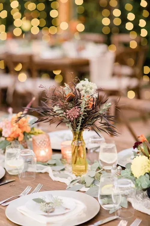 Elegant banquet table with floral centerpieces, candles, glassware, and warm string lights in the background