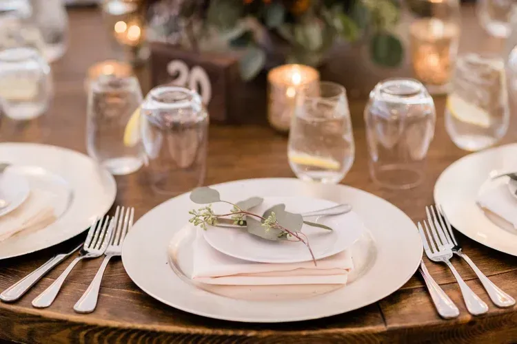 Elegant wedding reception table set with white plates, silverware, glassware, and candlelit decor