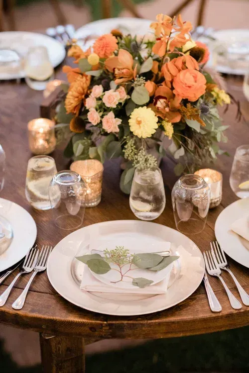 Elegant table setting with peach floral centerpiece, white plates, and gold candle holders