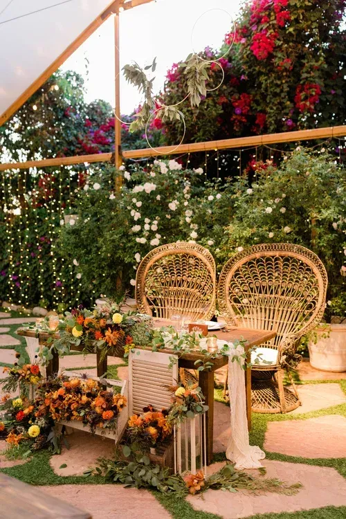 Garden seating area with wicker chairs, floral table decor, and lush greenery under pink bougainvillea.