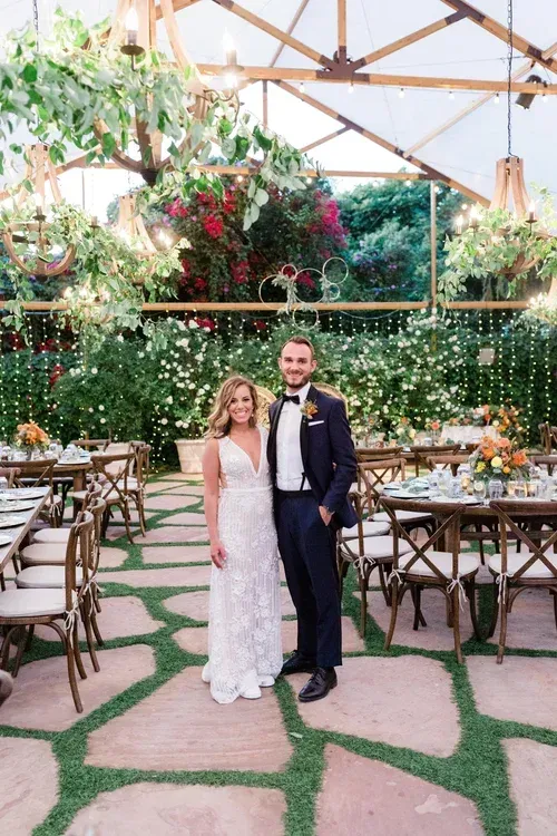 Couple posing in formal wear at an outdoor wedding reception under a floral canopy
