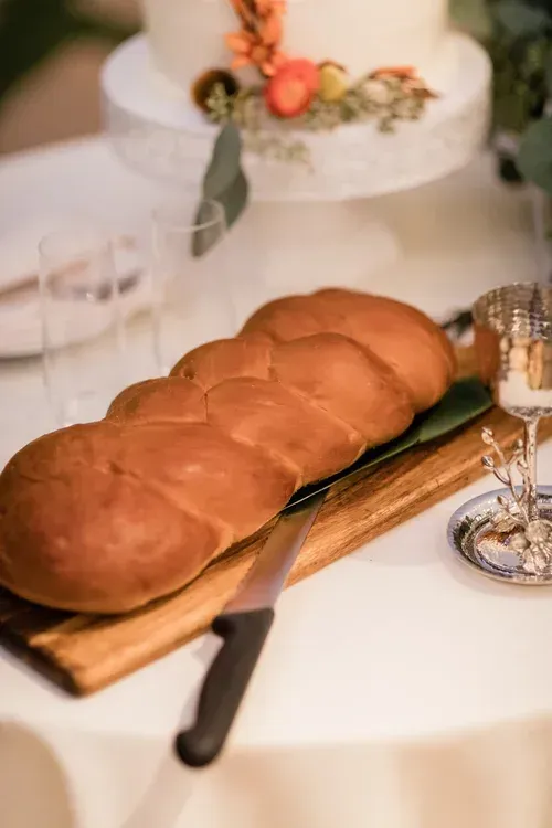 Round loaf bread on a wooden board at a table setting with candles and flowers