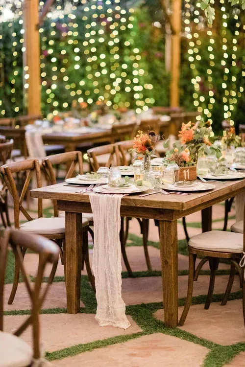 Outdoor dining table set with floral centerpiece, candles, and string lights in a warmly lit garden setting