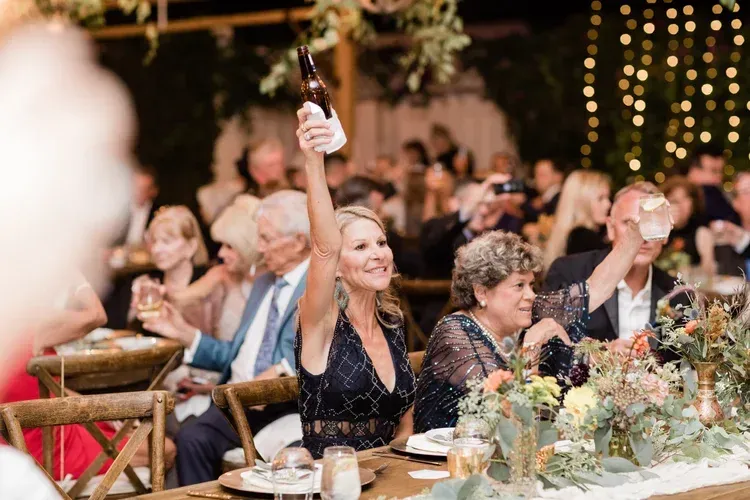 Guests at a candlelit outdoor dinner raise glasses in a celebratory toast.