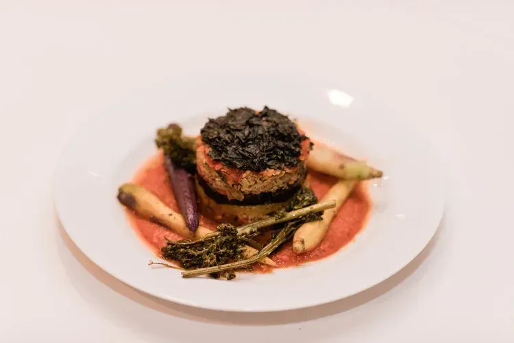 Gourmet plated dish with seared meat, vegetables, and red sauce on a white plate