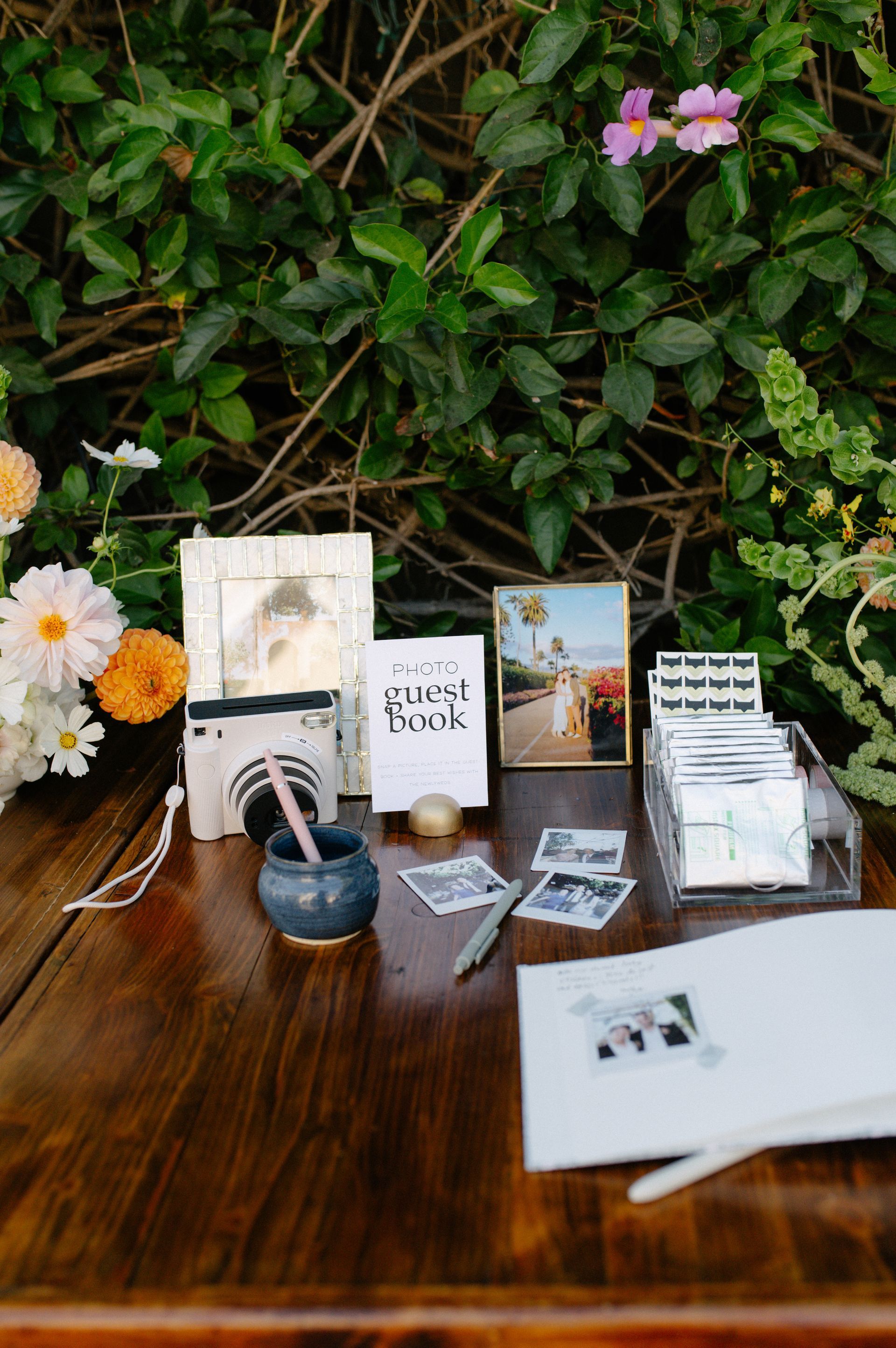 Wedding stationery display on a wooden table with cards, invitation proofs, and flowers against greenery.
