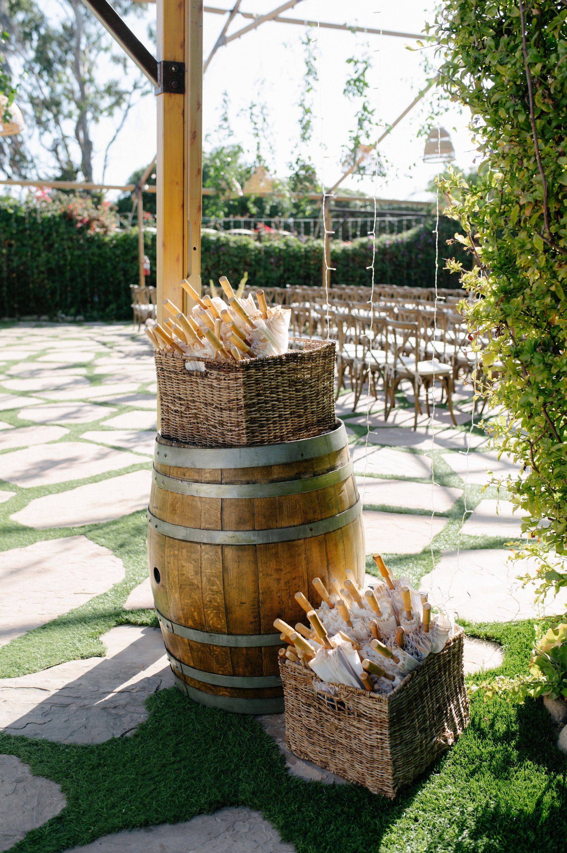 Rustic wooden barrels and baskets of bread on a sunlit patio with empty chairs and stone paving