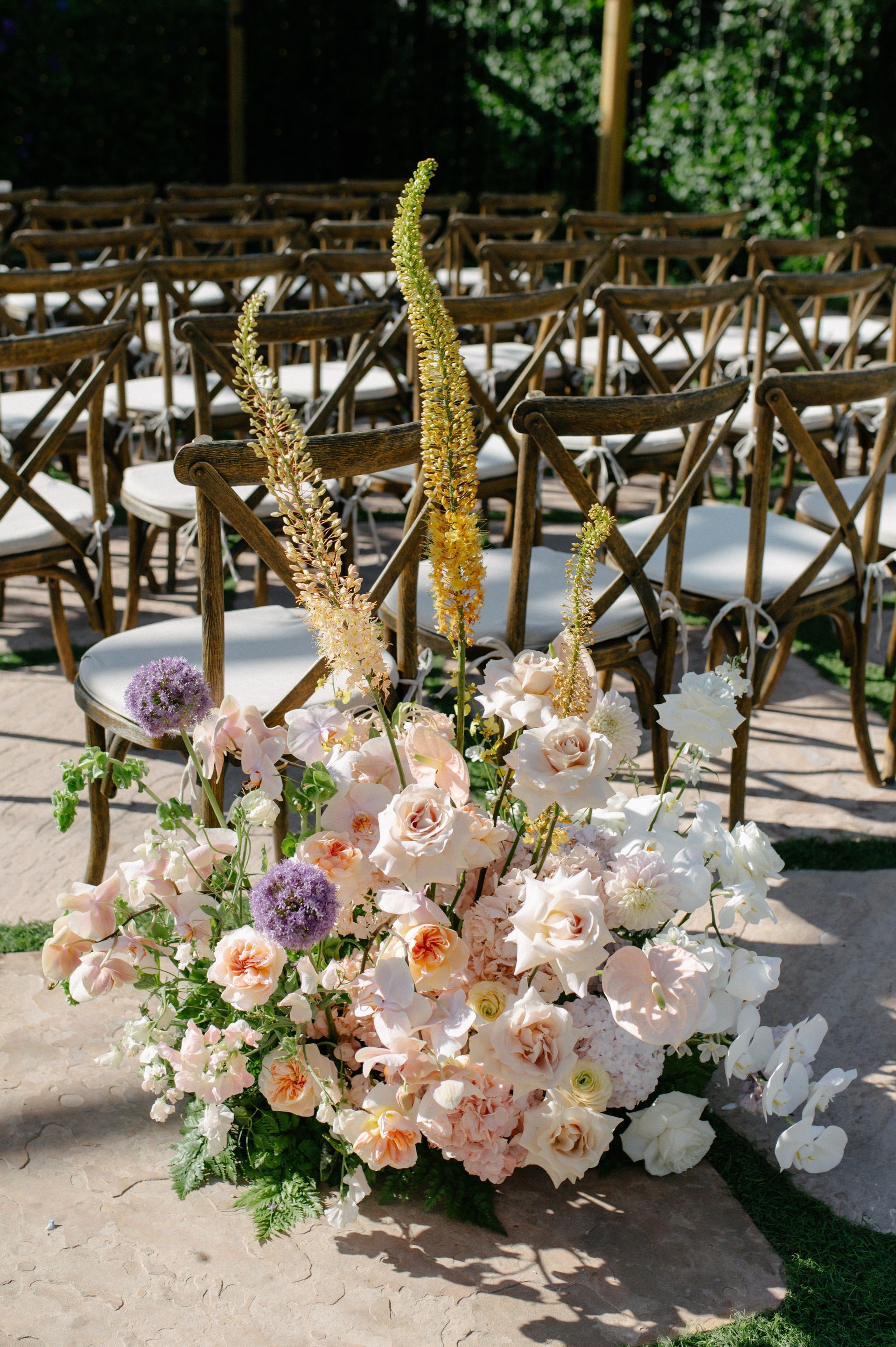 Pastel floral arrangement with white, pink, and peach blooms and tall gold stems at an outdoor event