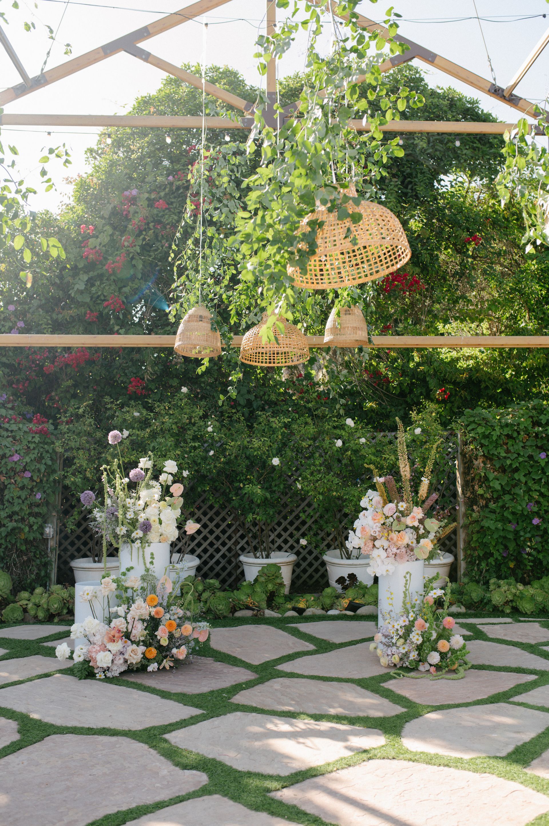 Floral wedding arch with white flower arrangements and hanging wicker baskets in a lush garden