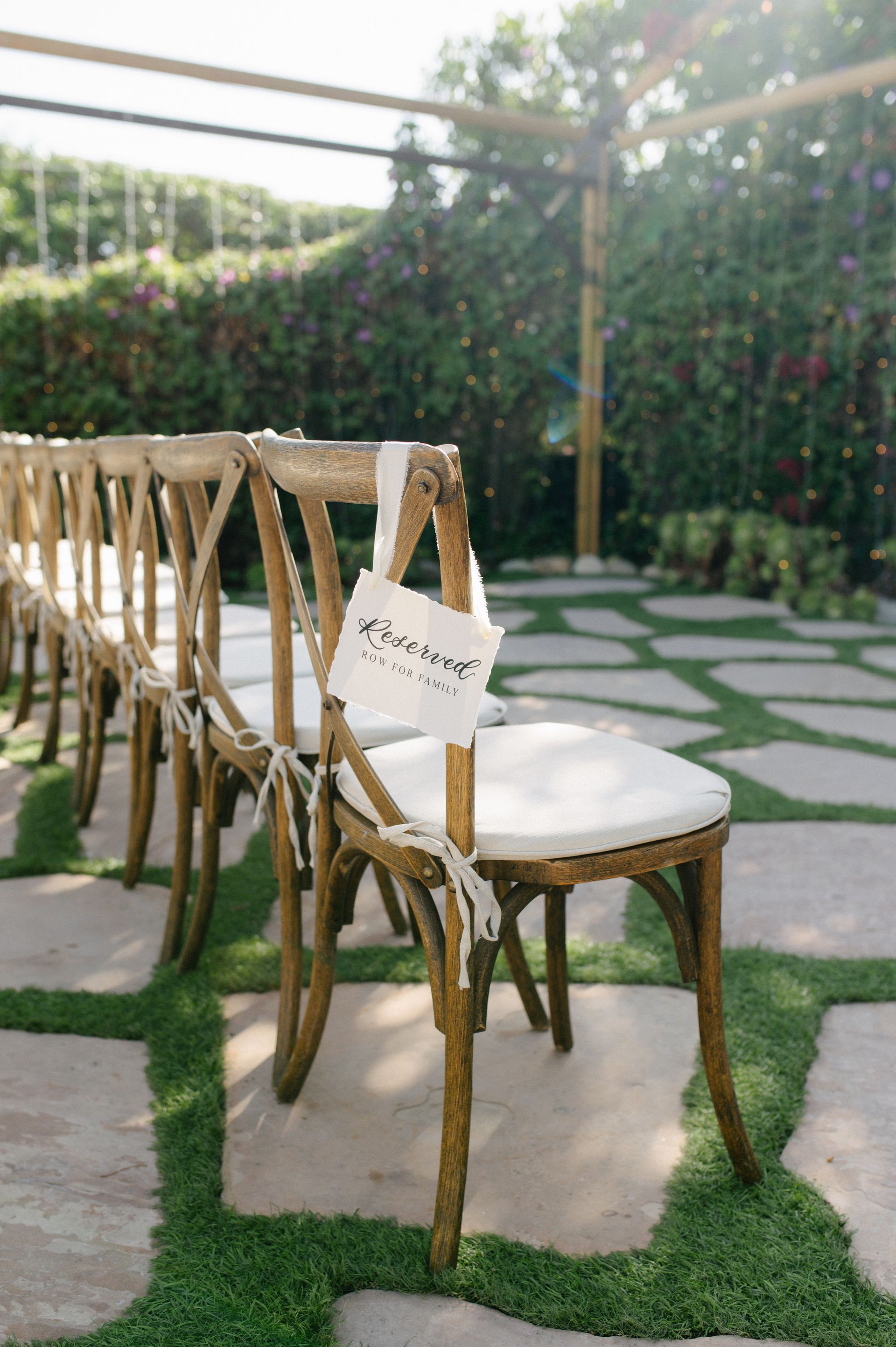 Row of gold chairs with white cushions on a stone patio in a garden setting