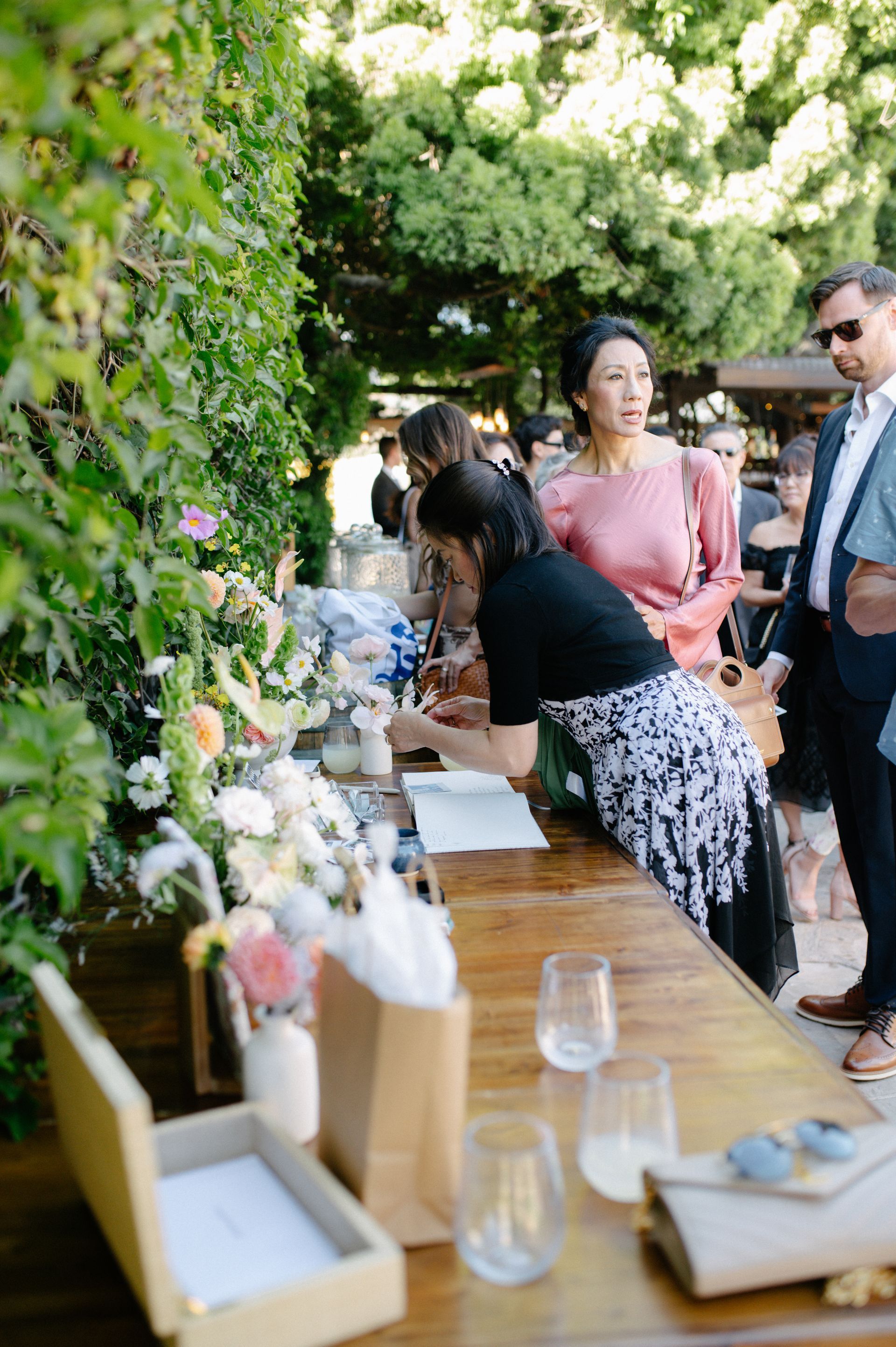 Outdoor garden gathering with people mingling beside a long table of flowers and glassware