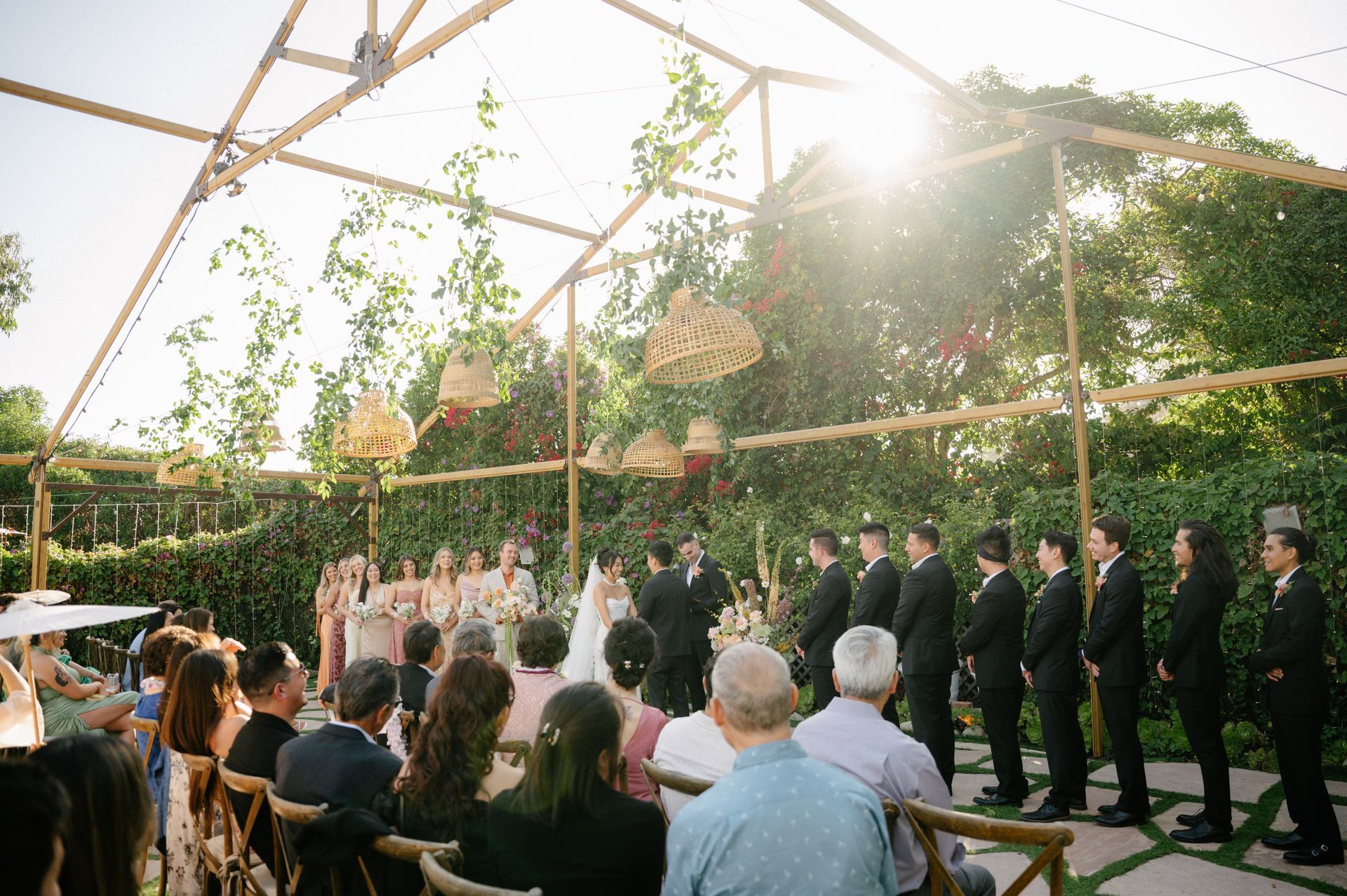 Outdoor wedding ceremony under a transparent tent, with bride and groom at the altar and guests seated nearby