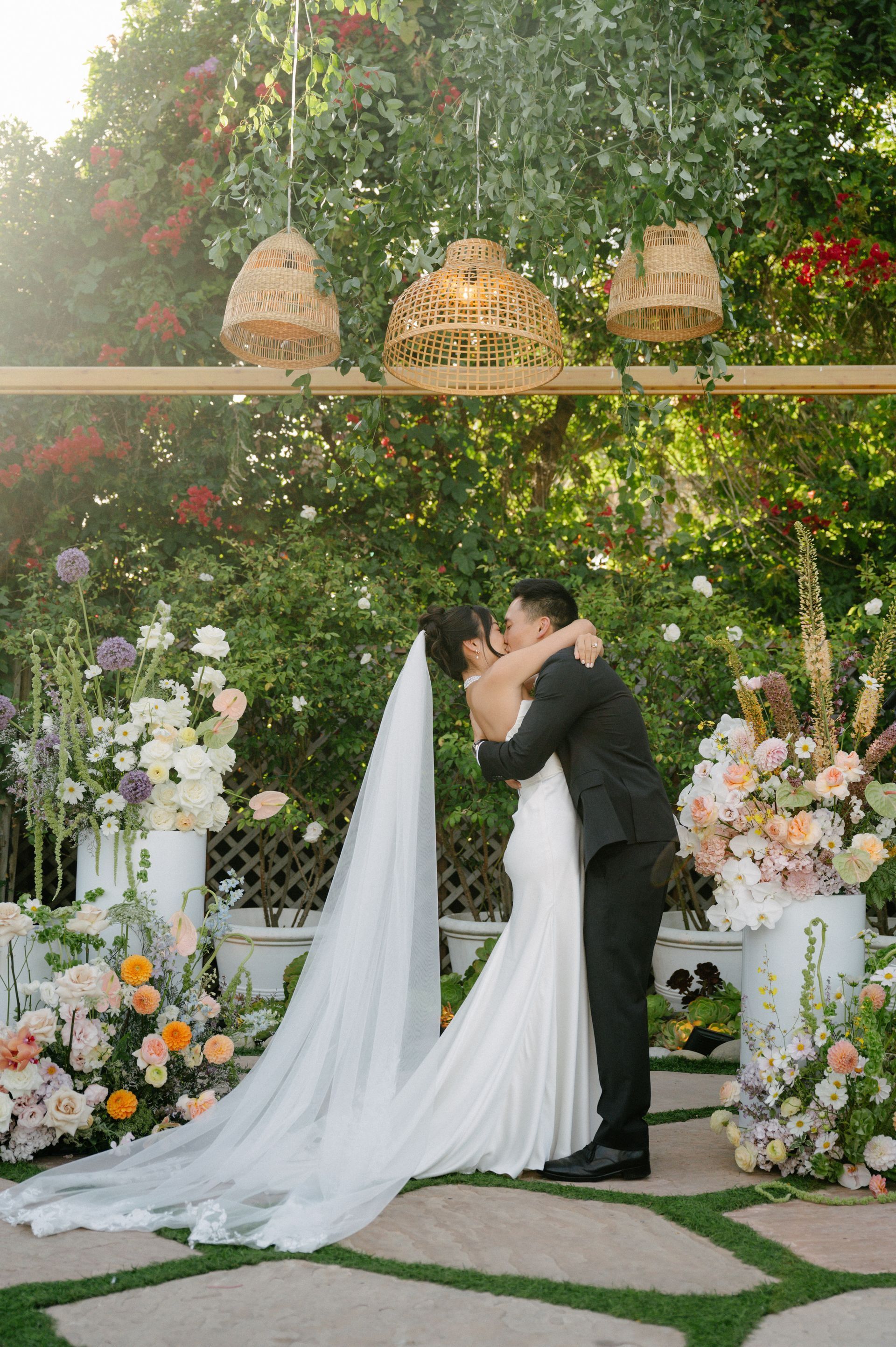 Bride and groom kissing under a floral arch in a garden wedding ceremony
